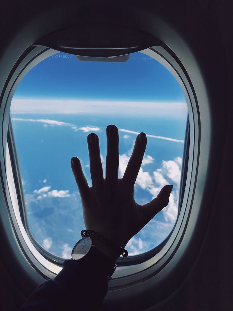 Photography of Person's Left Hand Touching an Airplane's Window jetlag sarah long-haul flight essentials